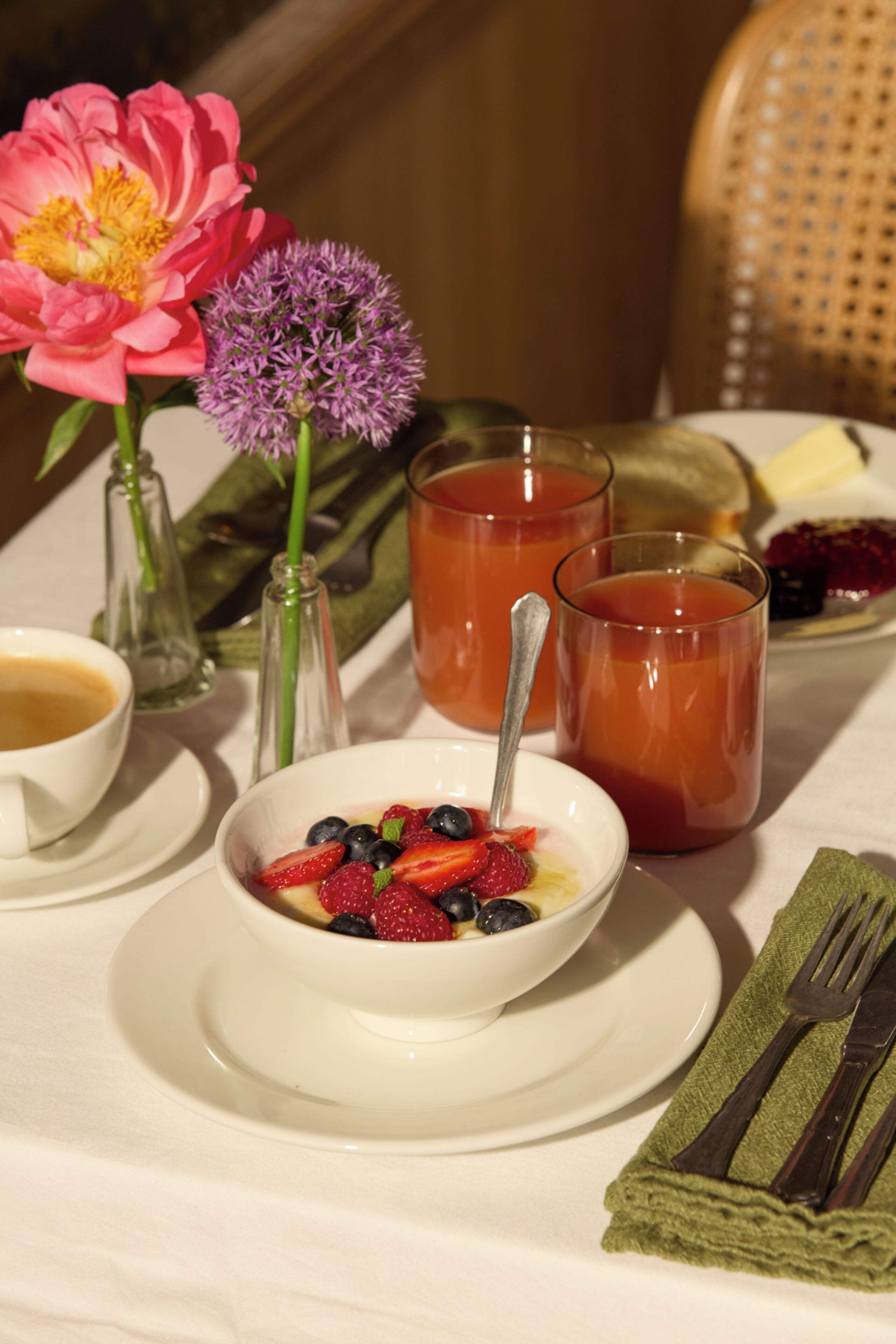 Ein Tisch mit einer Obstschale, zwei Gläsern rotem Getränk, einer Kaffeetasse und einer Blumenkomposition.