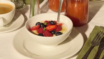 A table with a bowl of fruit, two glasses of red beverage, a cup of coffee, and a flower arrangement.