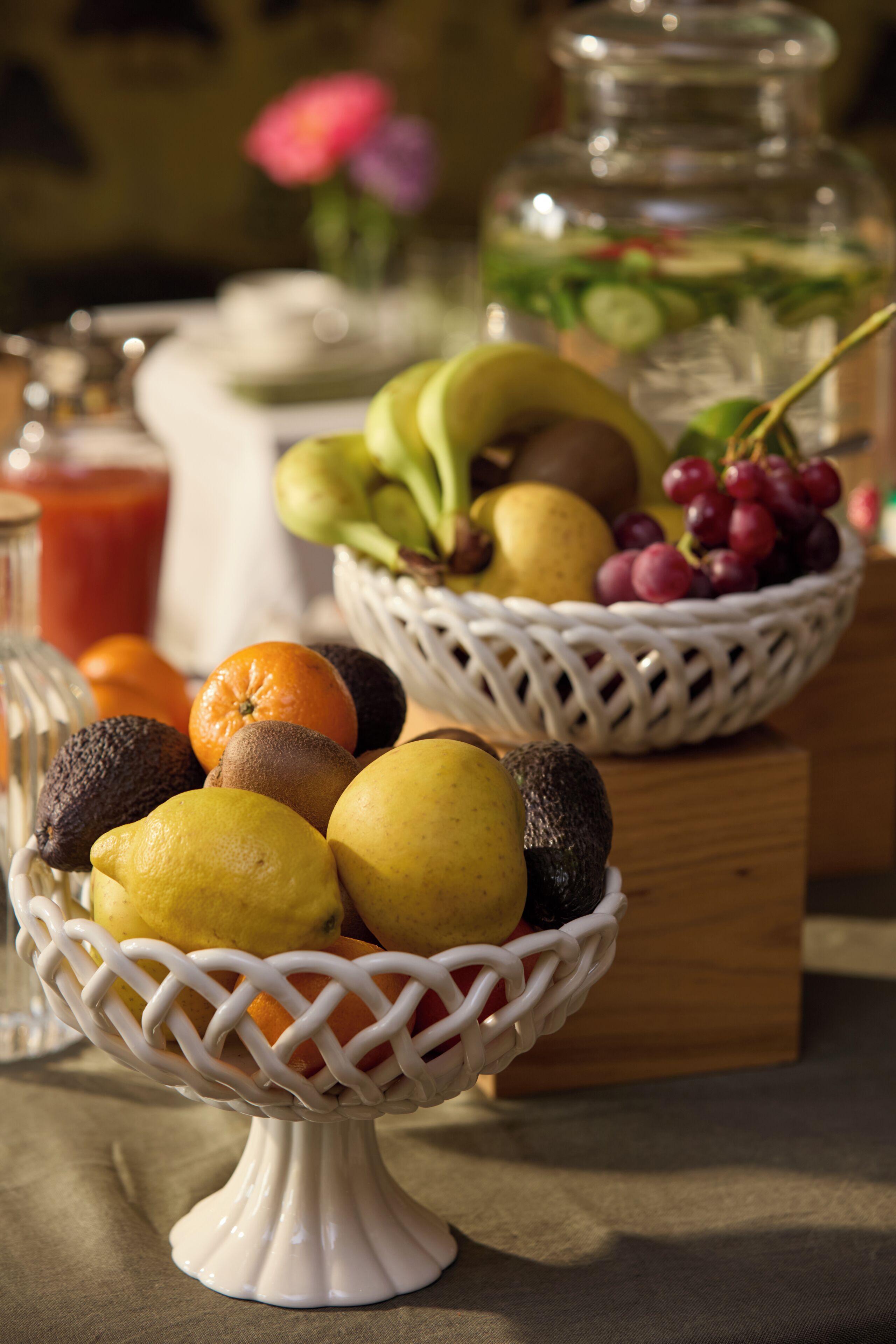 A fruit bowl on a table with a glass jar and a bottle in the background.