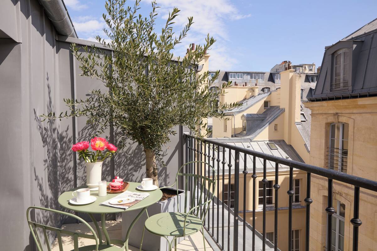 A balcony with a table, chairs, a potted plant, and a vase of flowers.