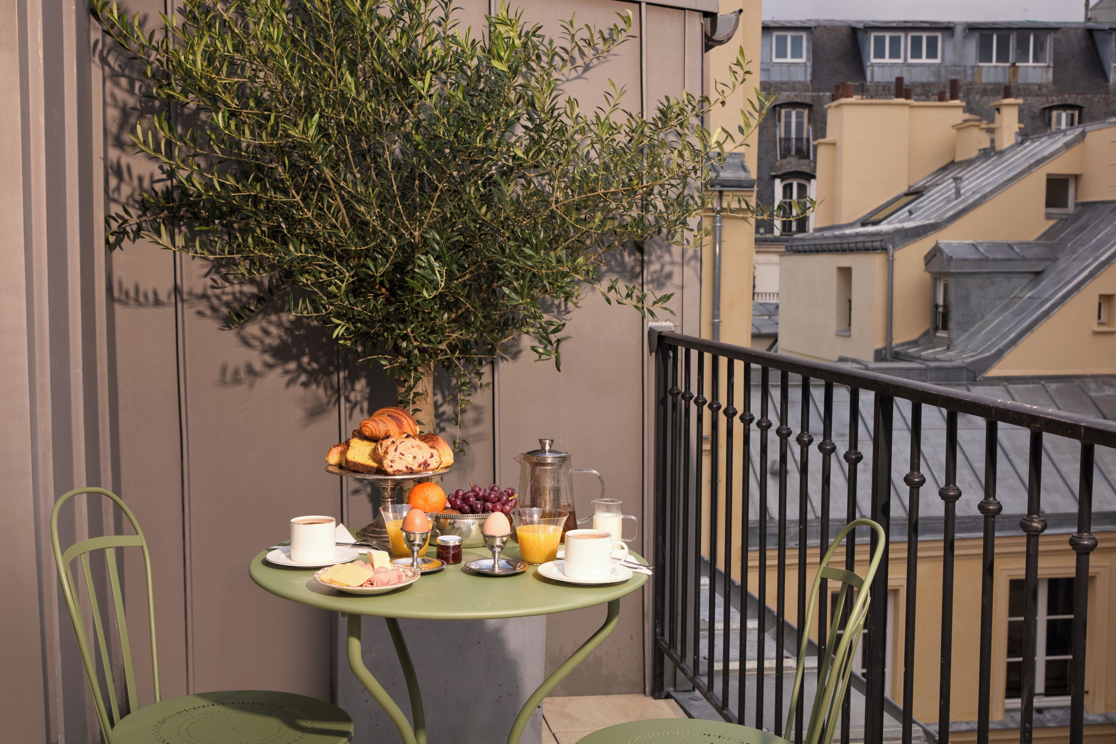 Un balcon avec une table préparée pour le petit-déjeuner, comprenant des croissants, des fruits et une cafetière.