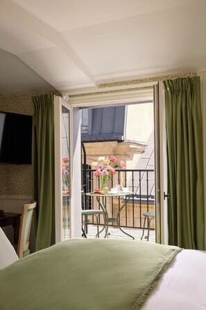 A hotel room with a balcony, a bed, a TV mounted on the wall, and a table with flowers. - Hôtel des Orfèvres (Paris)