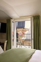 A hotel room with a balcony, a bed, a TV mounted on the wall, and a table with flowers.