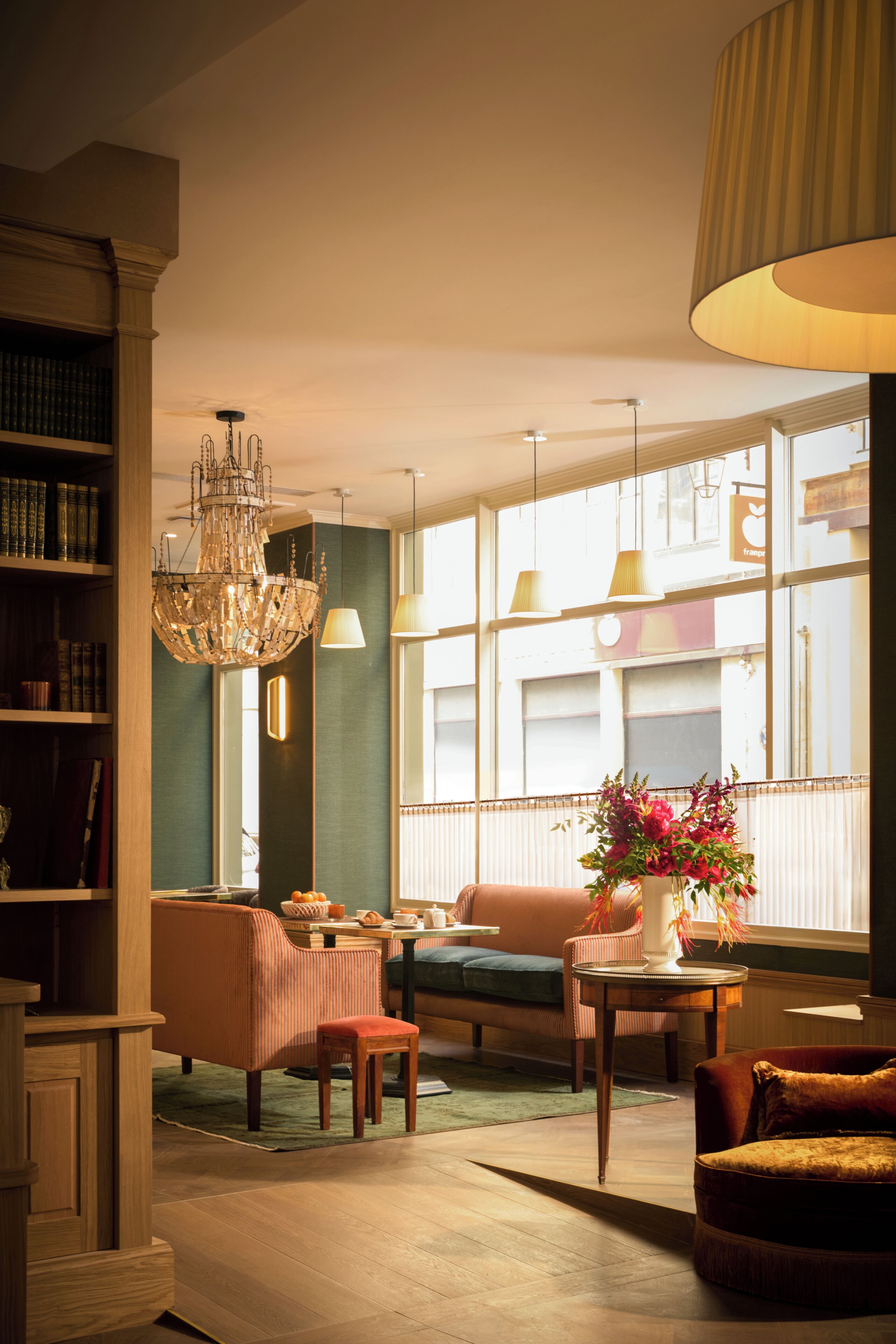 A well-lit living room with a chandelier, a bookshelf, a sofa, and a table with a vase of flowers.