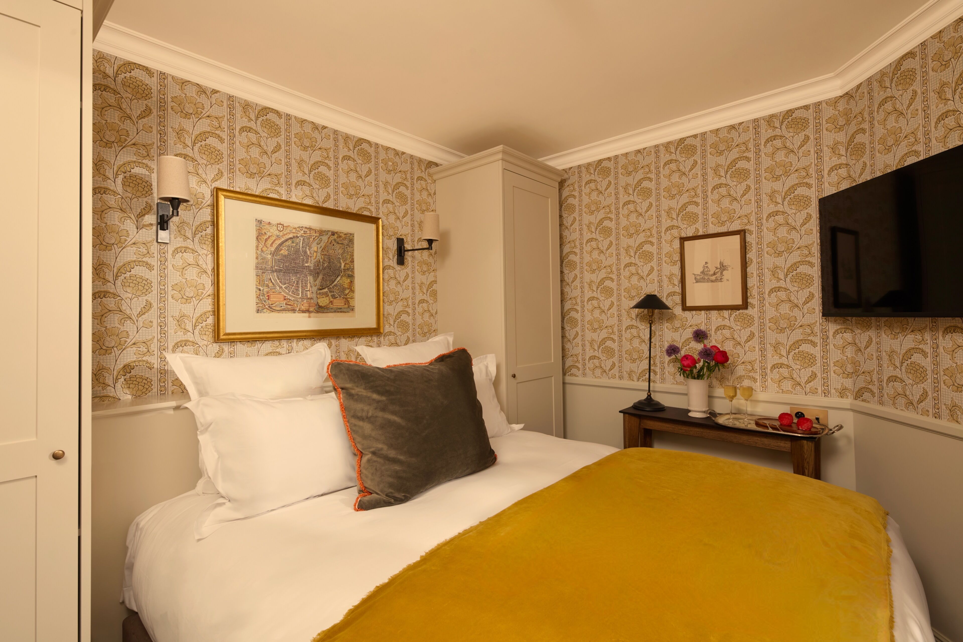 A hotel room with a bed, a nightstand, a TV, and a framed picture on the wall.