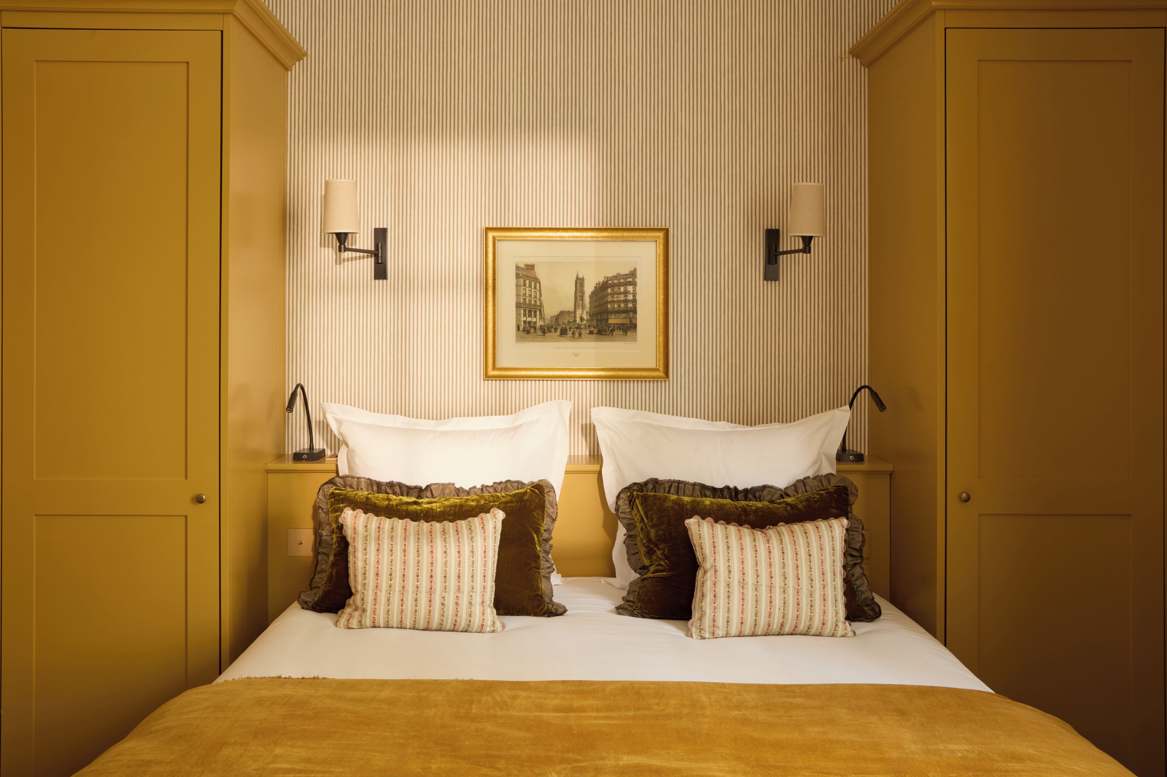 A hotel room with a bed, two bedside tables, a framed picture on the wall, and two wall-mounted lamps.