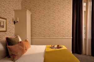 A hotel room with a bed, a bedside table with a tray of breakfast items, a wall-mounted lamp, and a framed picture.