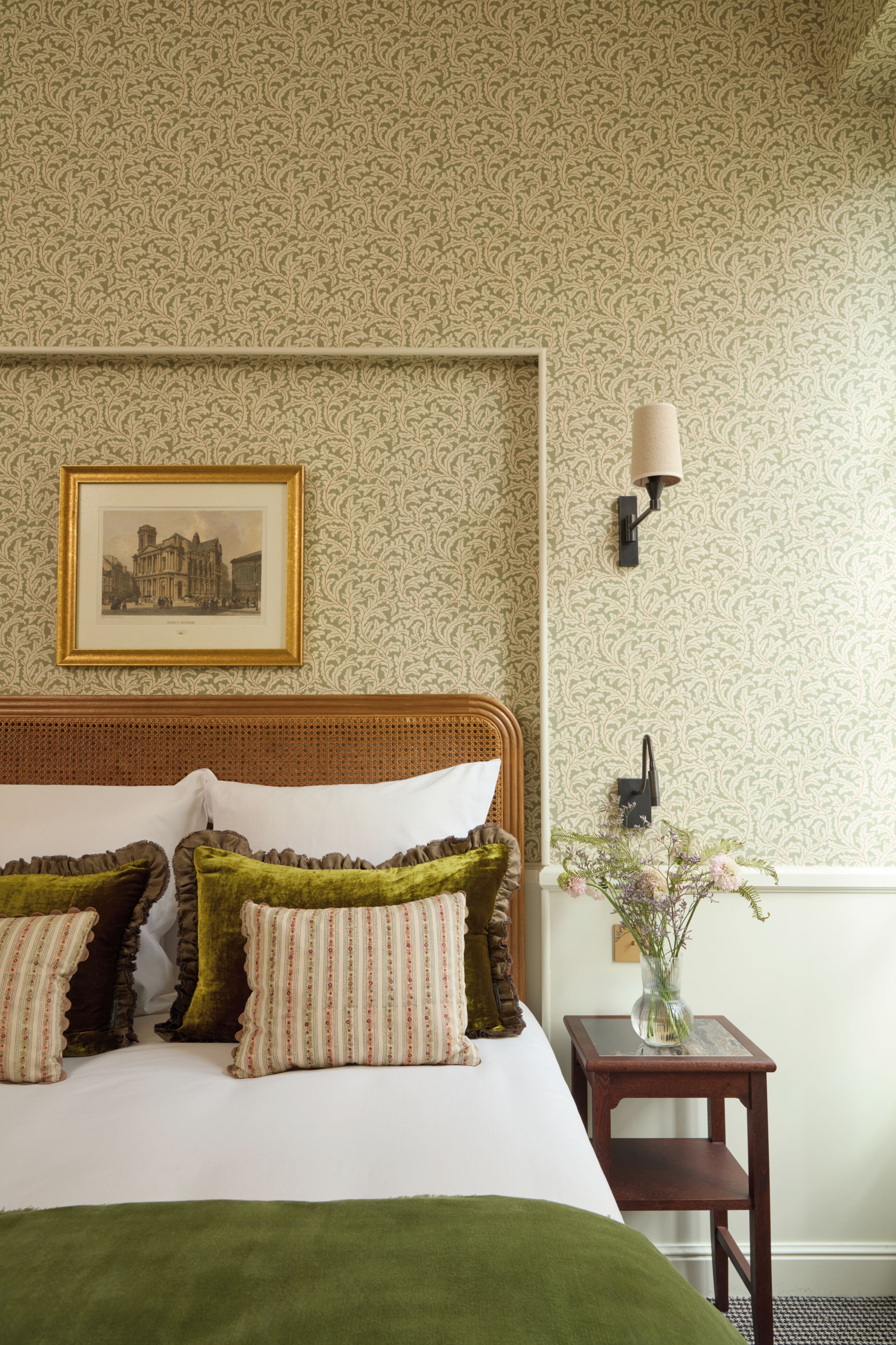 A neatly made bed with pillows, a framed picture on the wall, and a small table with a vase.