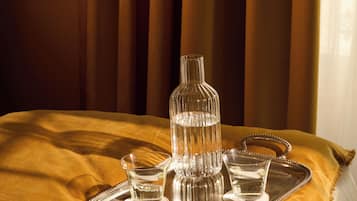 Una cama con un atril que contiene una botella de vidrio, dos vasos y una taza.