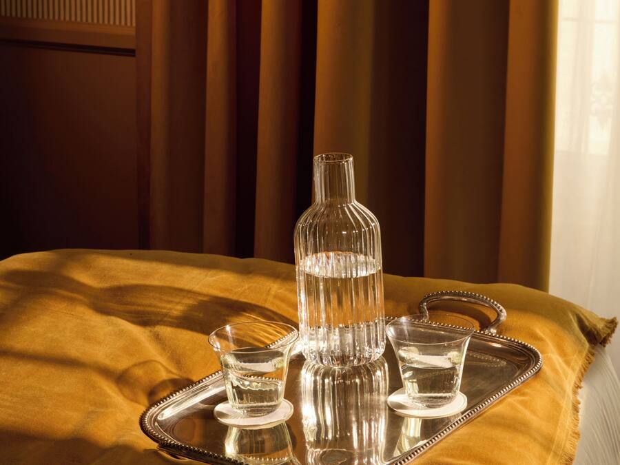 Una cama con un atril que contiene una botella de vidrio, dos vasos y una taza.