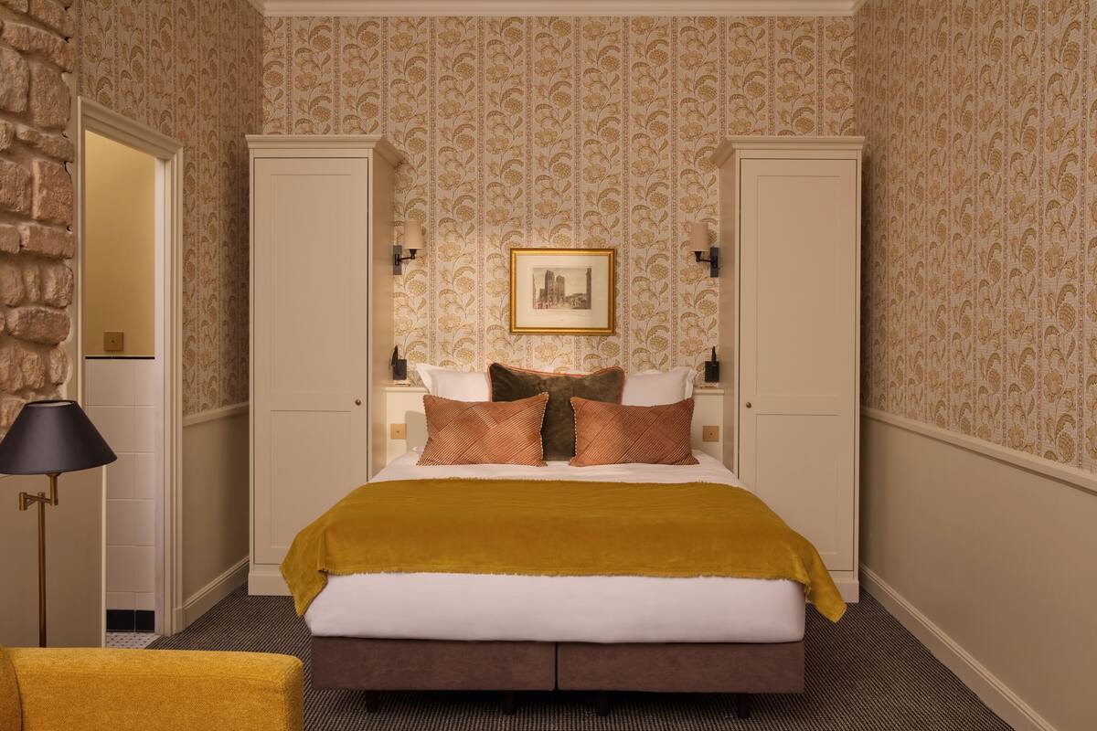 A hotel room with a bed, a nightstand, a lamp, and a wardrobe.