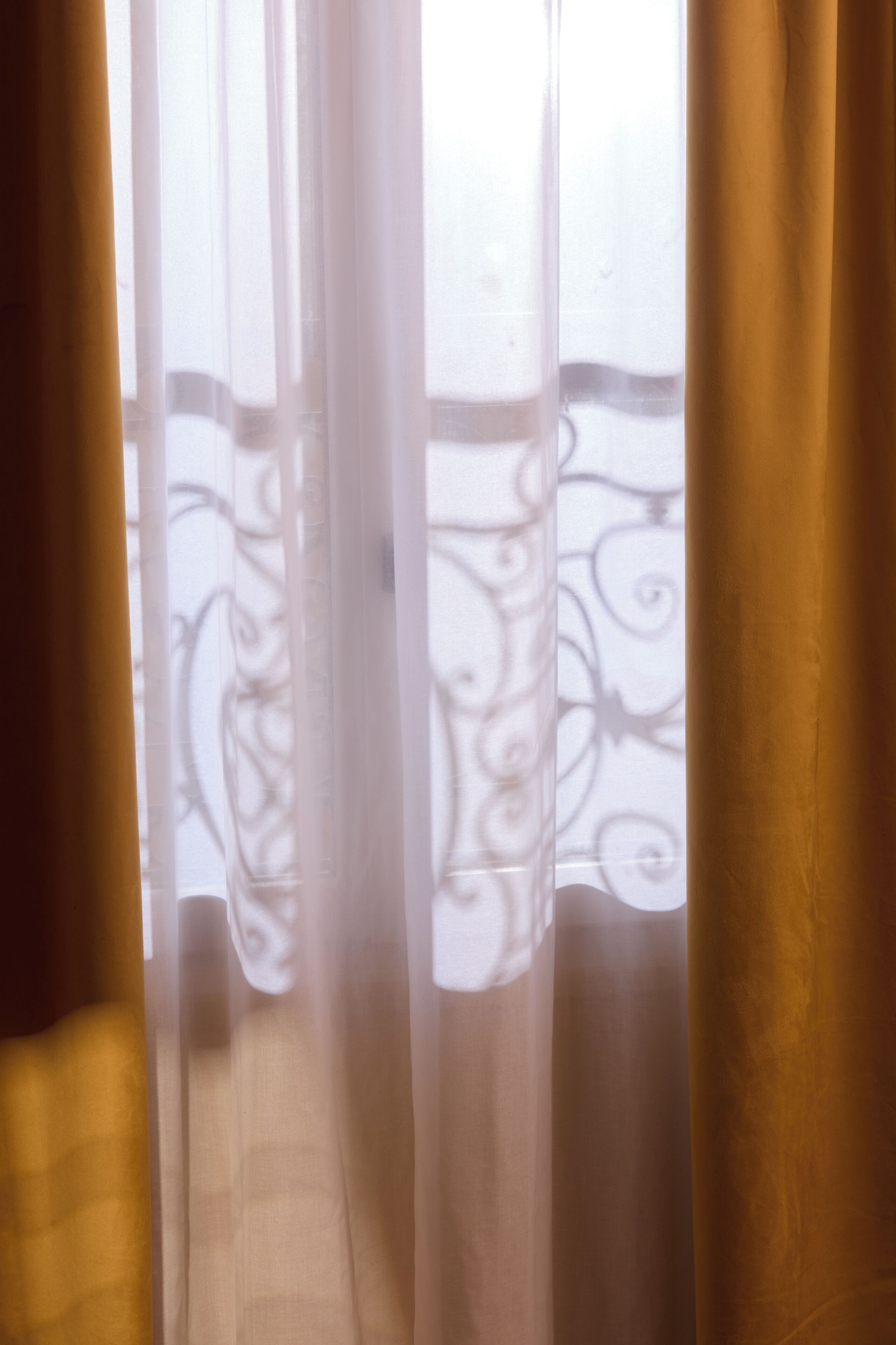 A view through sheer curtains with a balcony railing.