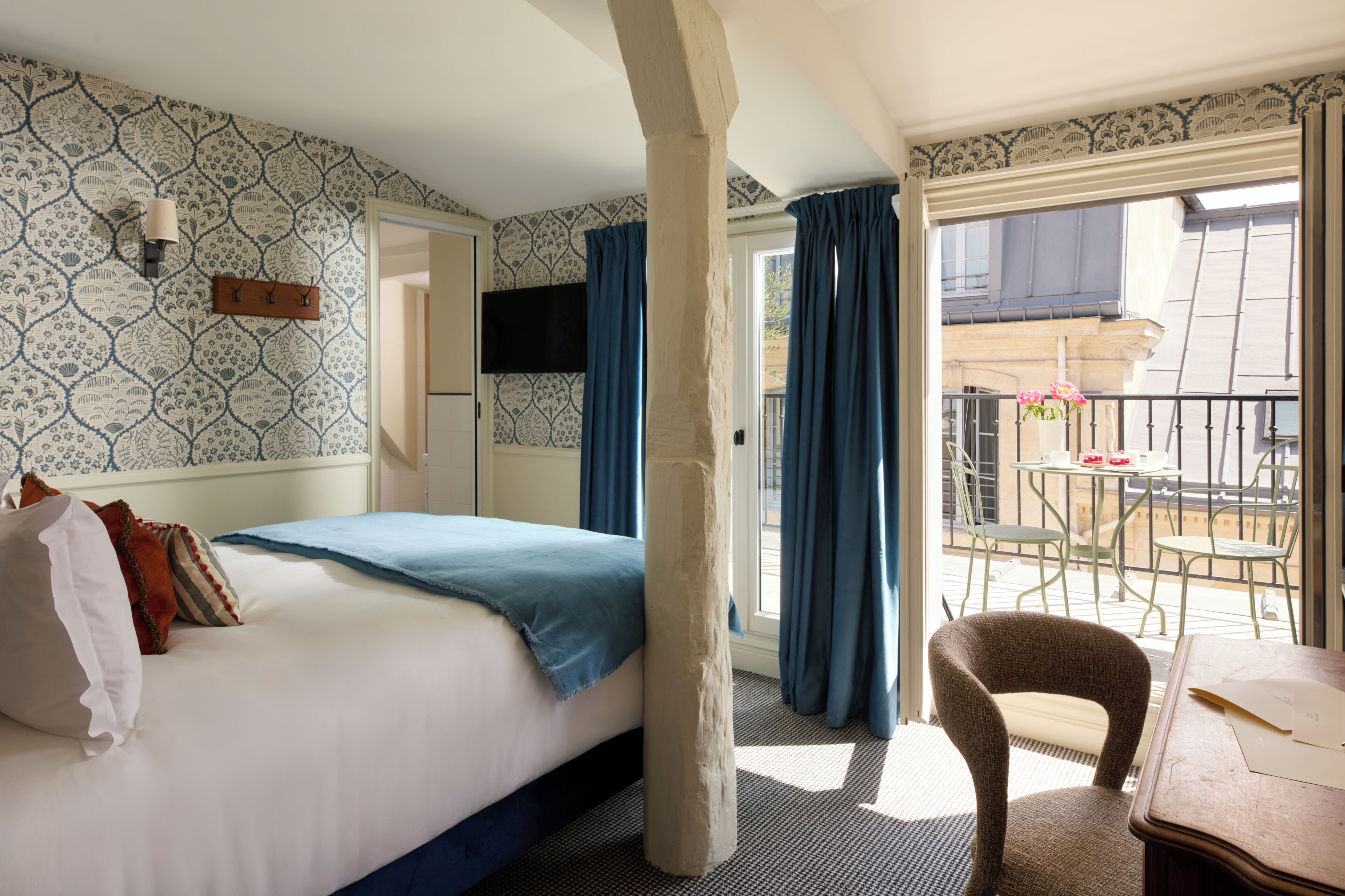 A hotel room with a bed, a chair, a table, and a balcony with a view.