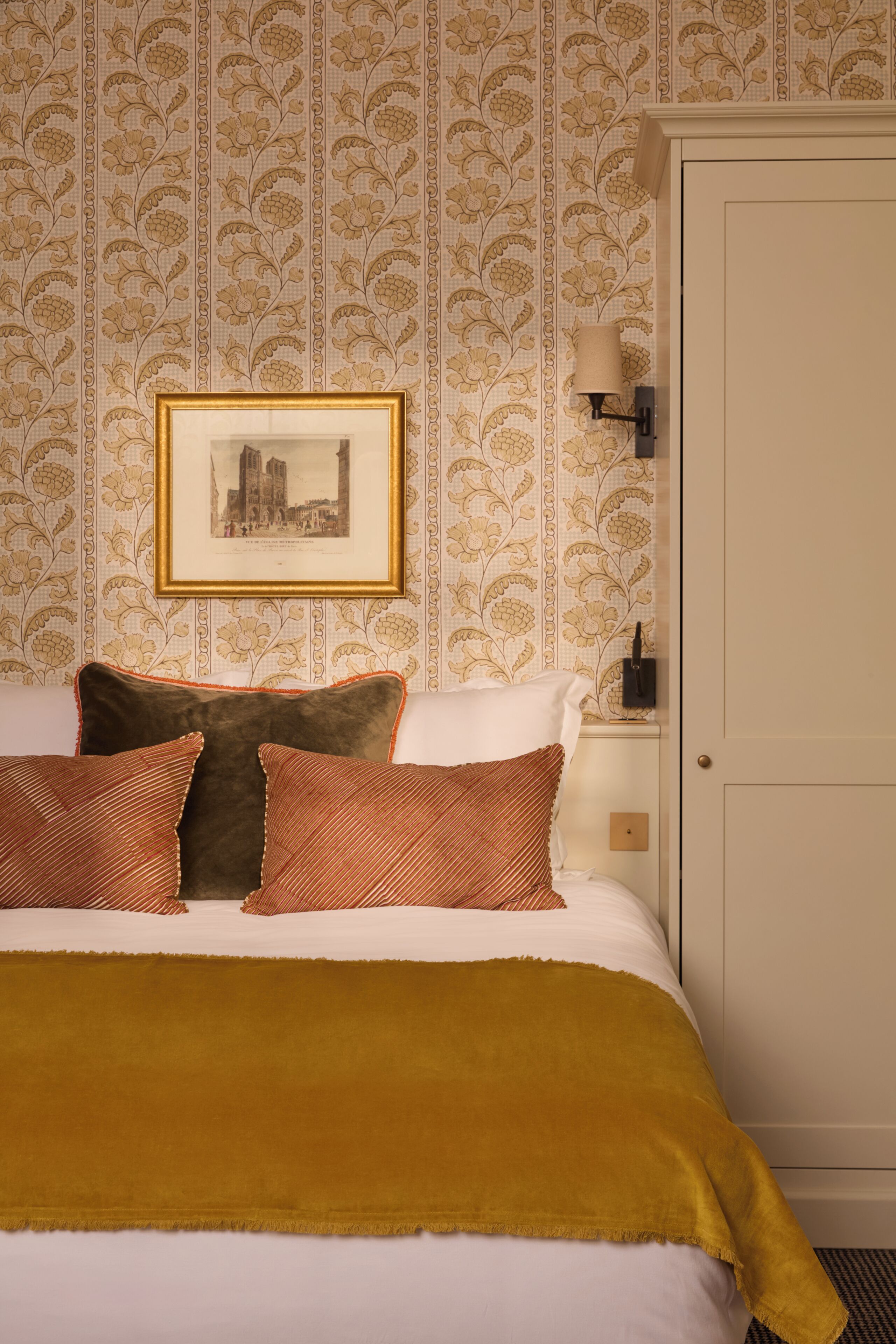 A neatly made bed with a framed picture above it, a bedside lamp, and a door to the right.