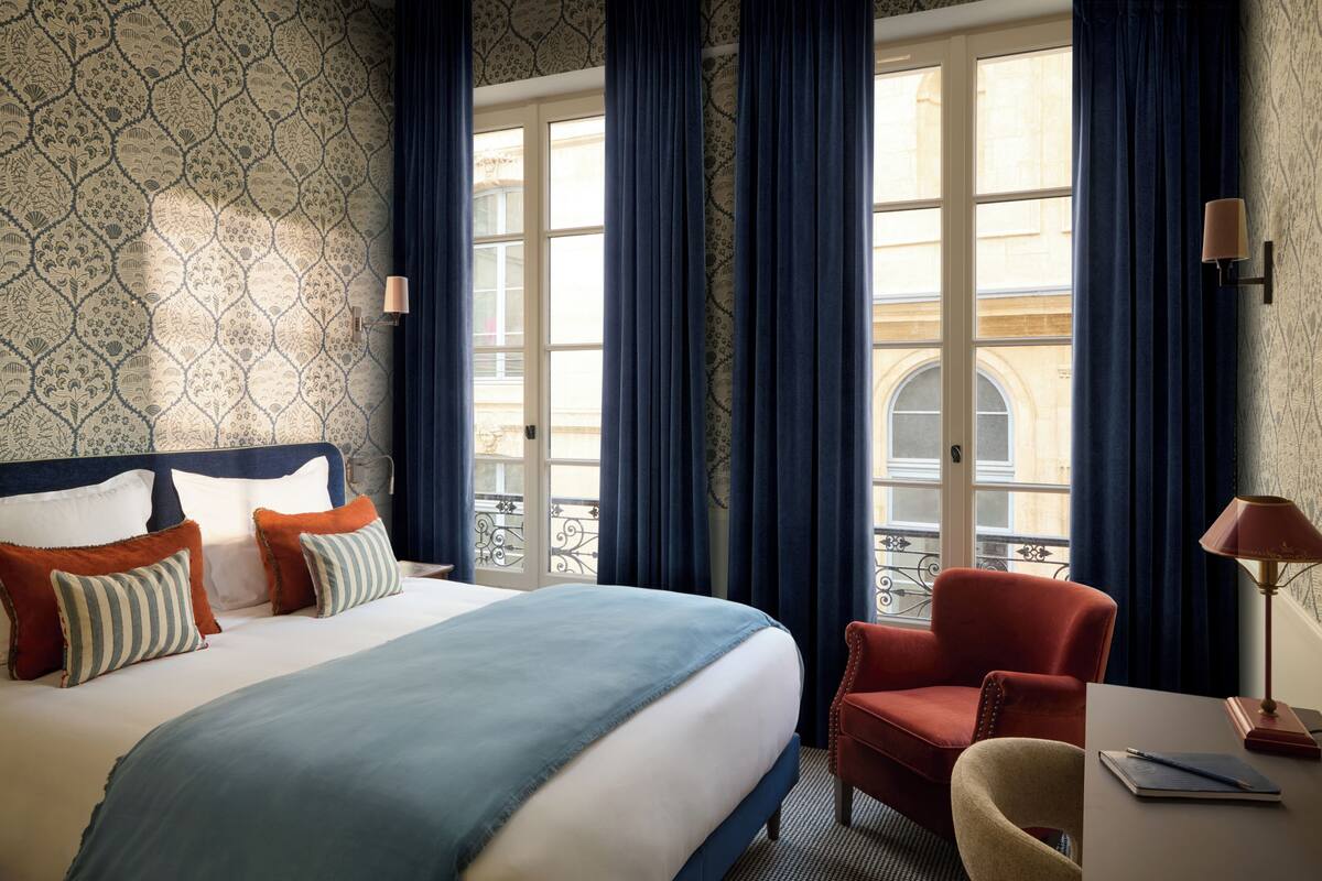 A hotel room with a bed, a chair, a desk, and a view of the outside.