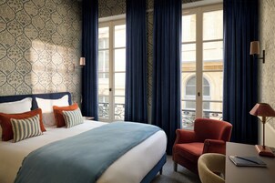 A hotel room with a bed, a chair, a desk, and a view of the outside.