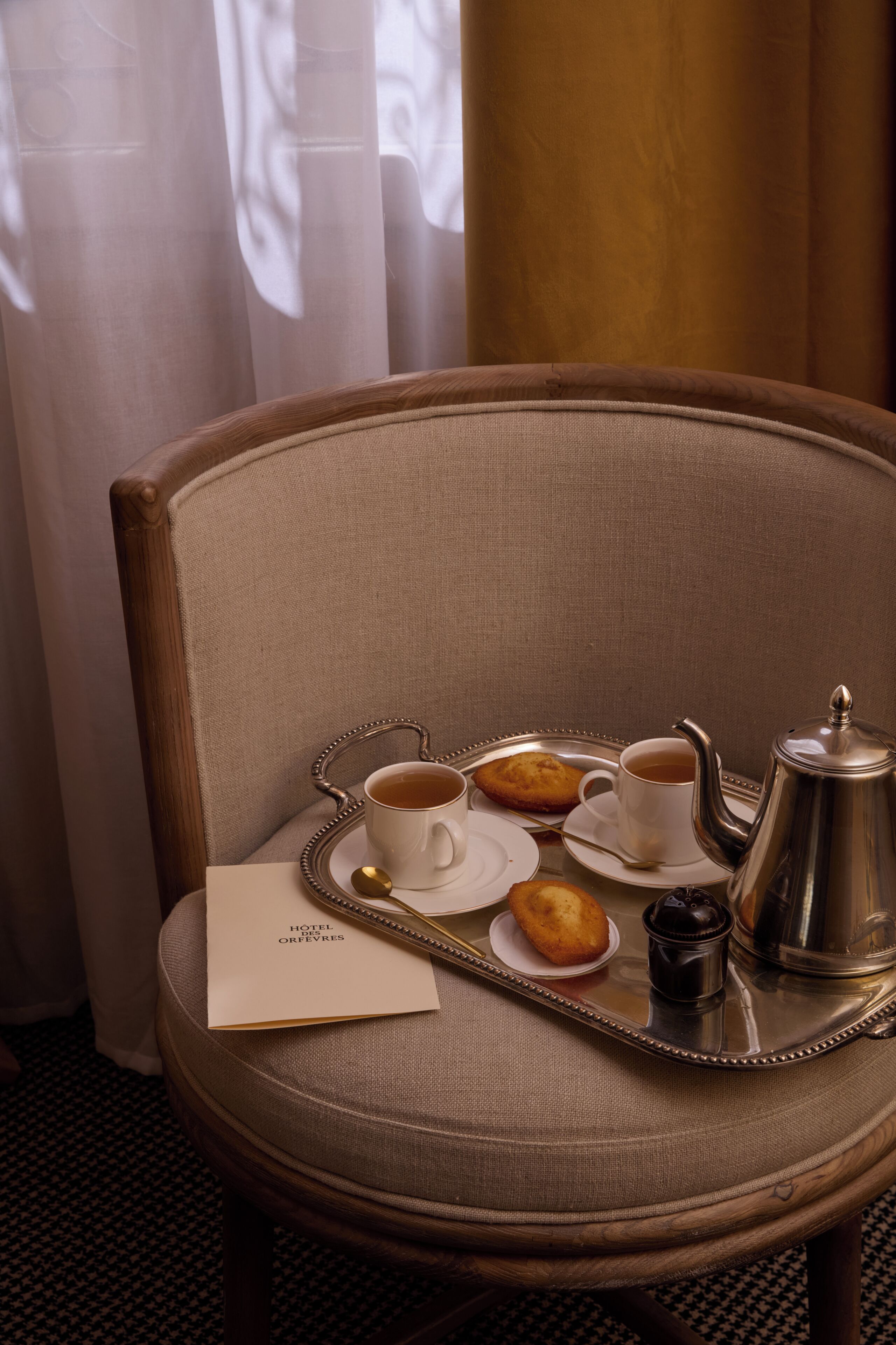 A hotel room with a dining table set for breakfast, including a tray with a teapot, cups, and pastries.