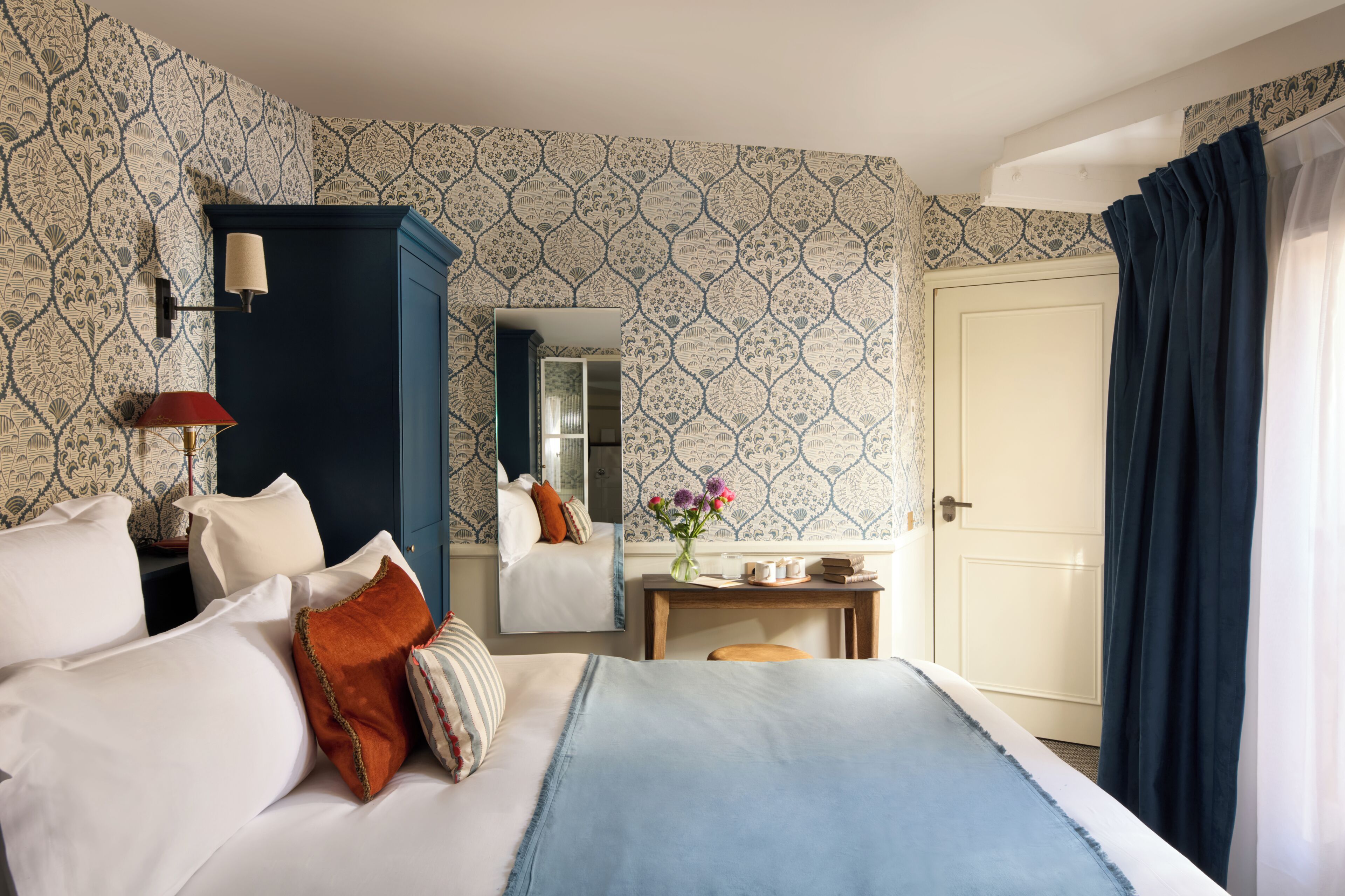 A hotel room with a bed, a nightstand, a mirror, a desk, and a door.
