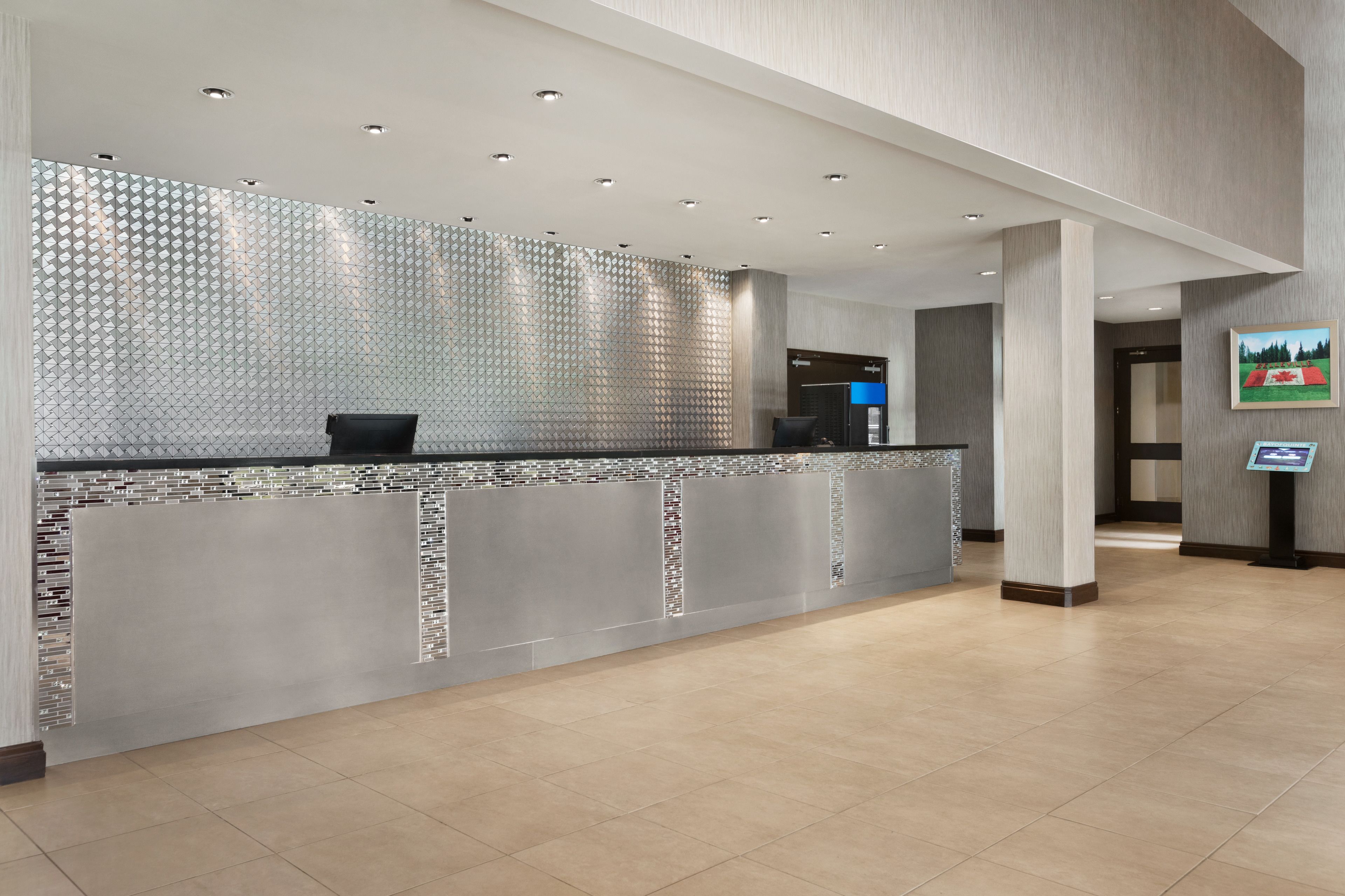 Un área de recepción moderna con un panel de vidrio, mostrador de recepción y quiosco de información digital.
