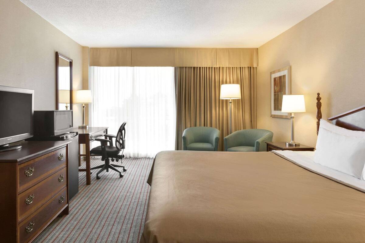 Une chambre d’hôtel avec un grand lit, un bureau avec une chaise, une télévision et deux lampes.