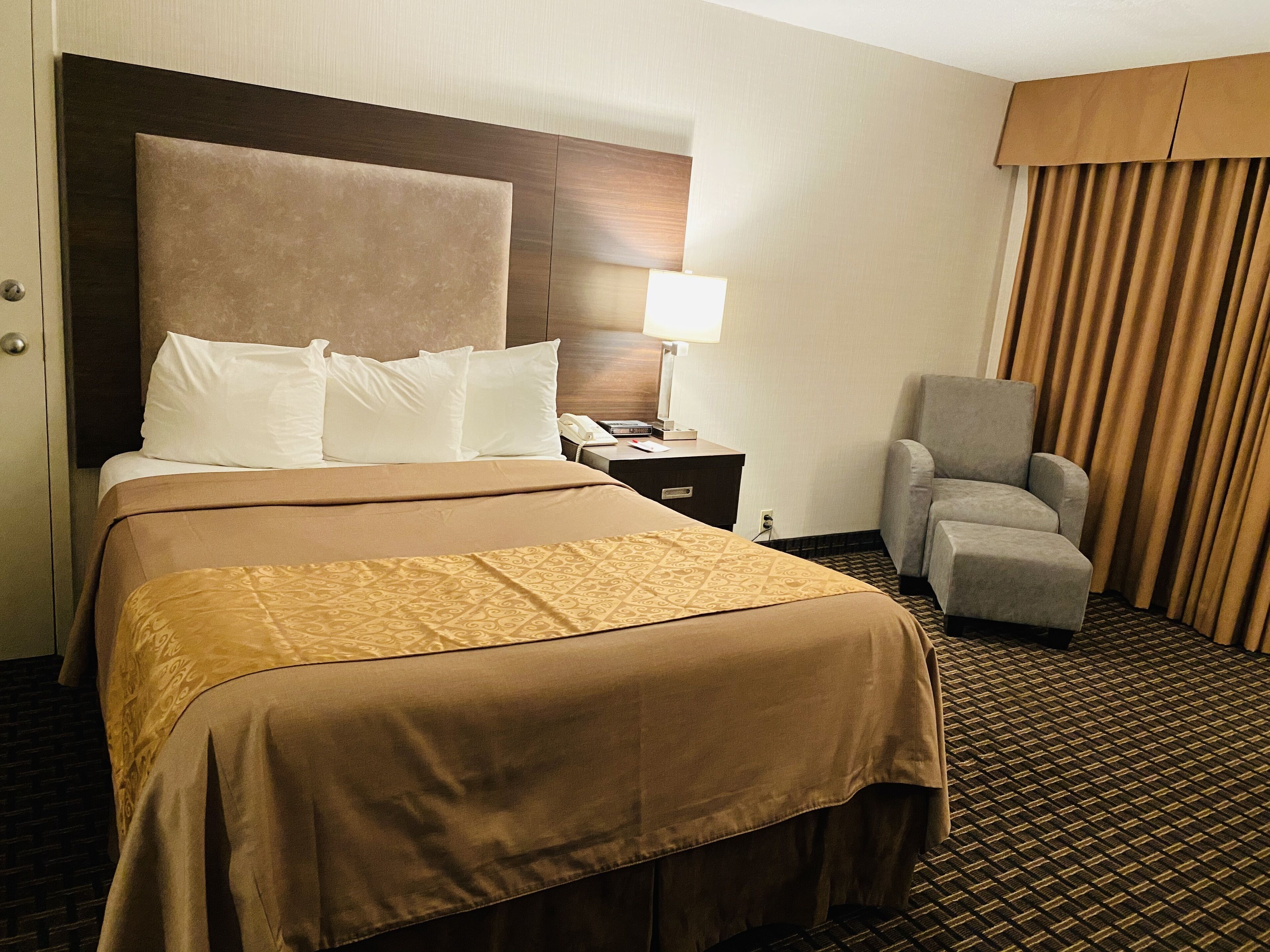 A hotel room with a large bed, a desk with a lamp, a chair, and a window with curtains.