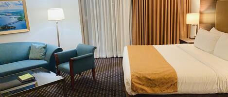 Ett hotellrum med en säng, en soffa, en stol, ett skrivbord, en lampa och en tavla på väggen.
