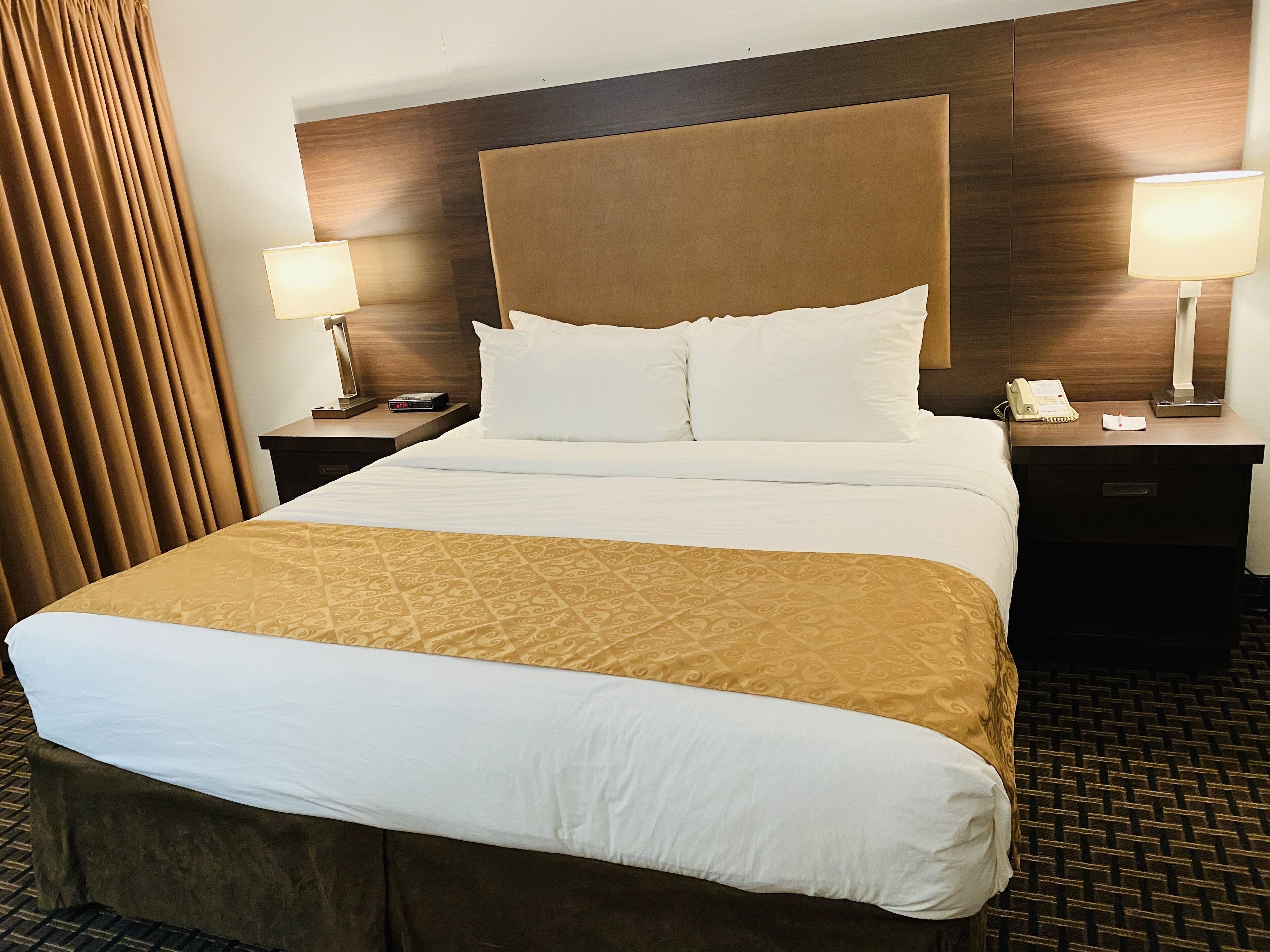 Une chambre d’hôtel avec un grand lit, deux tables de chevet, un téléphone et une lampe sur chaque table.