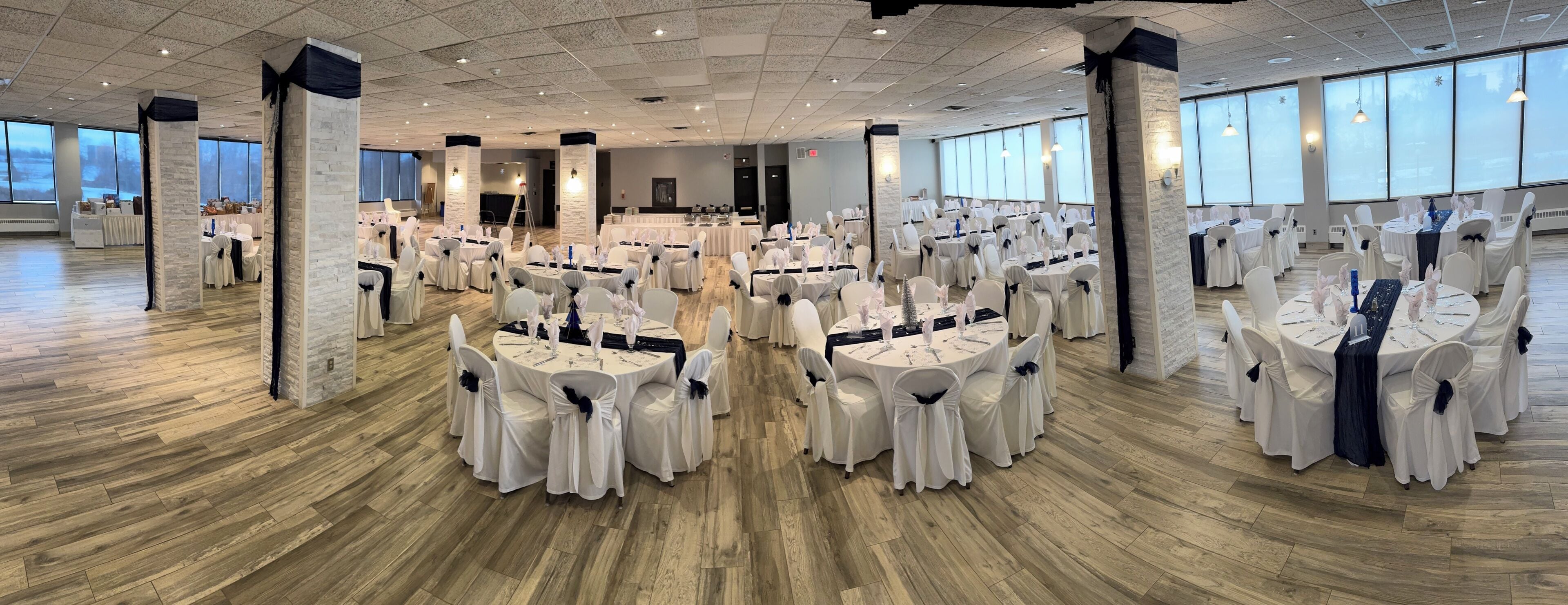 A spacious banquet hall with round tables, white chairs, and a wooden floor.