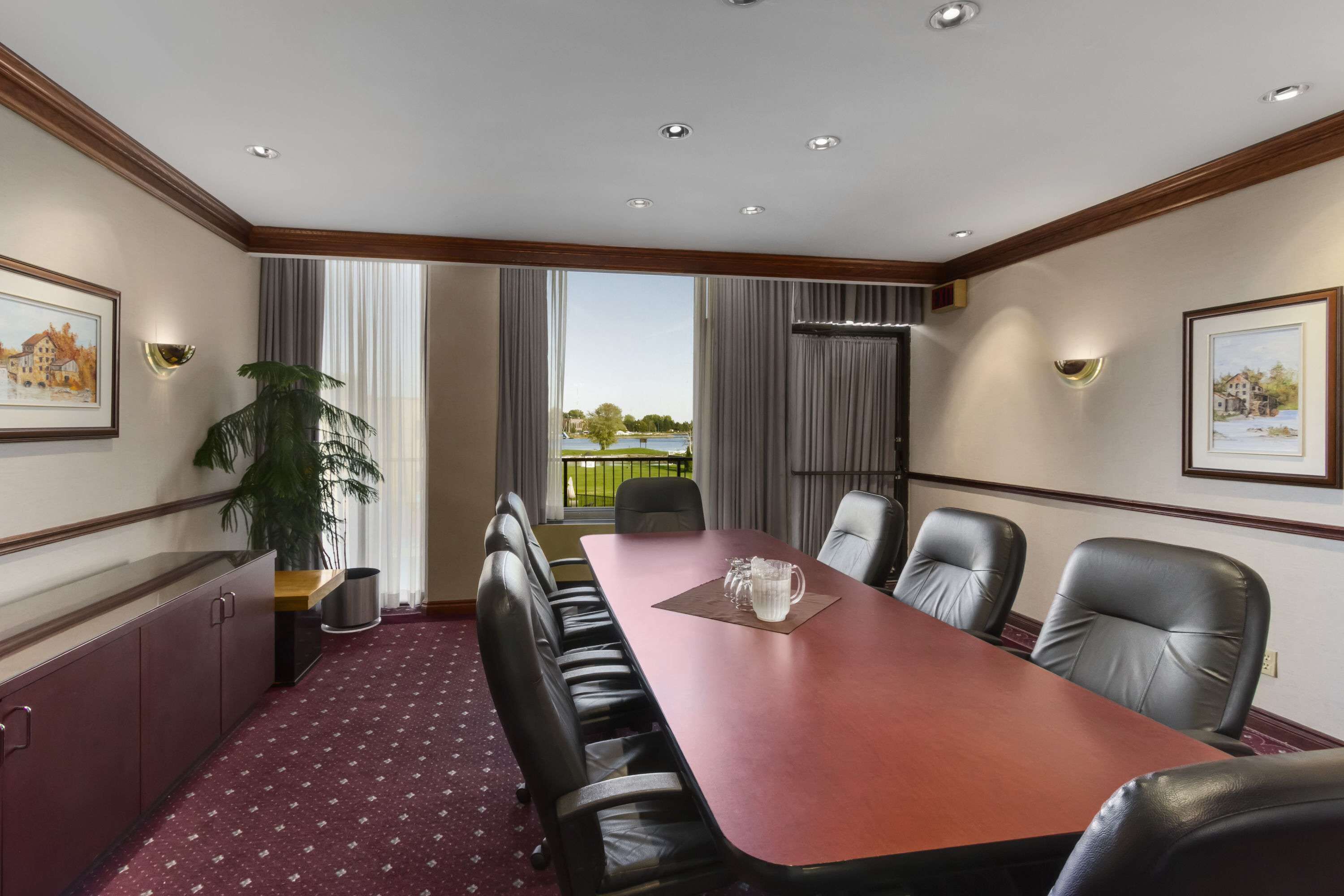 Un salón de conferencias con una larga mesa, sillas de cuero, una planta en maceta y obras de arte enmarcadas en las paredes.