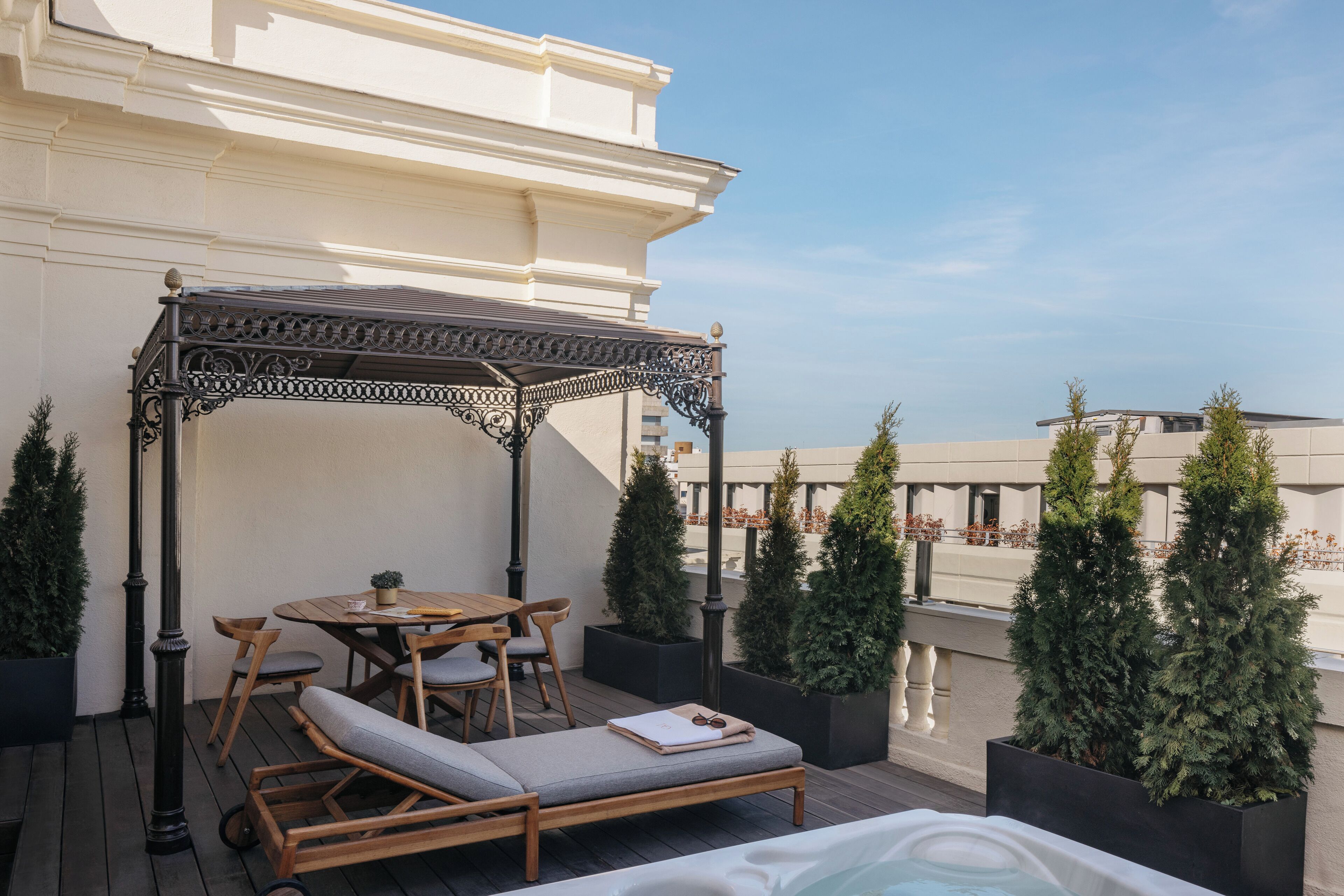 Una terraza en la azotea con mesa de madera, sillas, zona de estar con cojines y un jacuzzi.