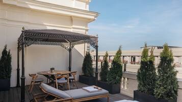 Una terraza en la azotea con mesa de madera, sillas, zona de estar con cojines y un jacuzzi.