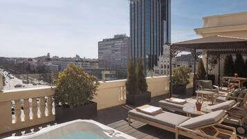 A rooftop terrace with lounge chairs, a hot tub, and potted plants.
