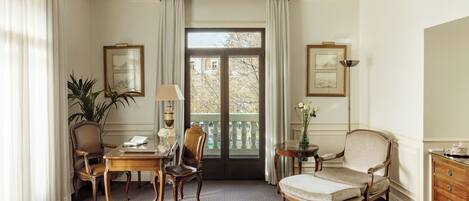 A well-lit room with a large window, a dining table with chairs, a sofa, and a wooden cabinet.