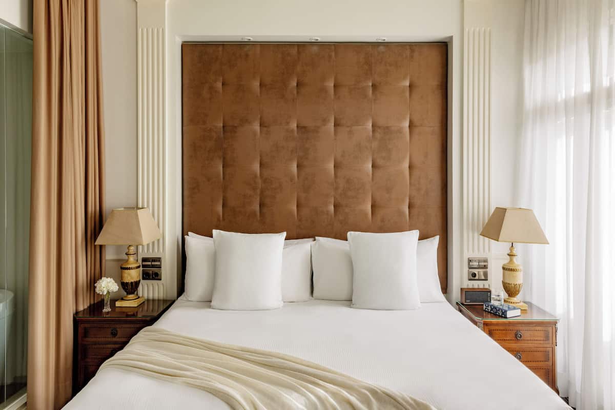 Une chambre d’hôtel avec un grand lit, deux tables de chevet, une tête de lit en bois et des rideaux.