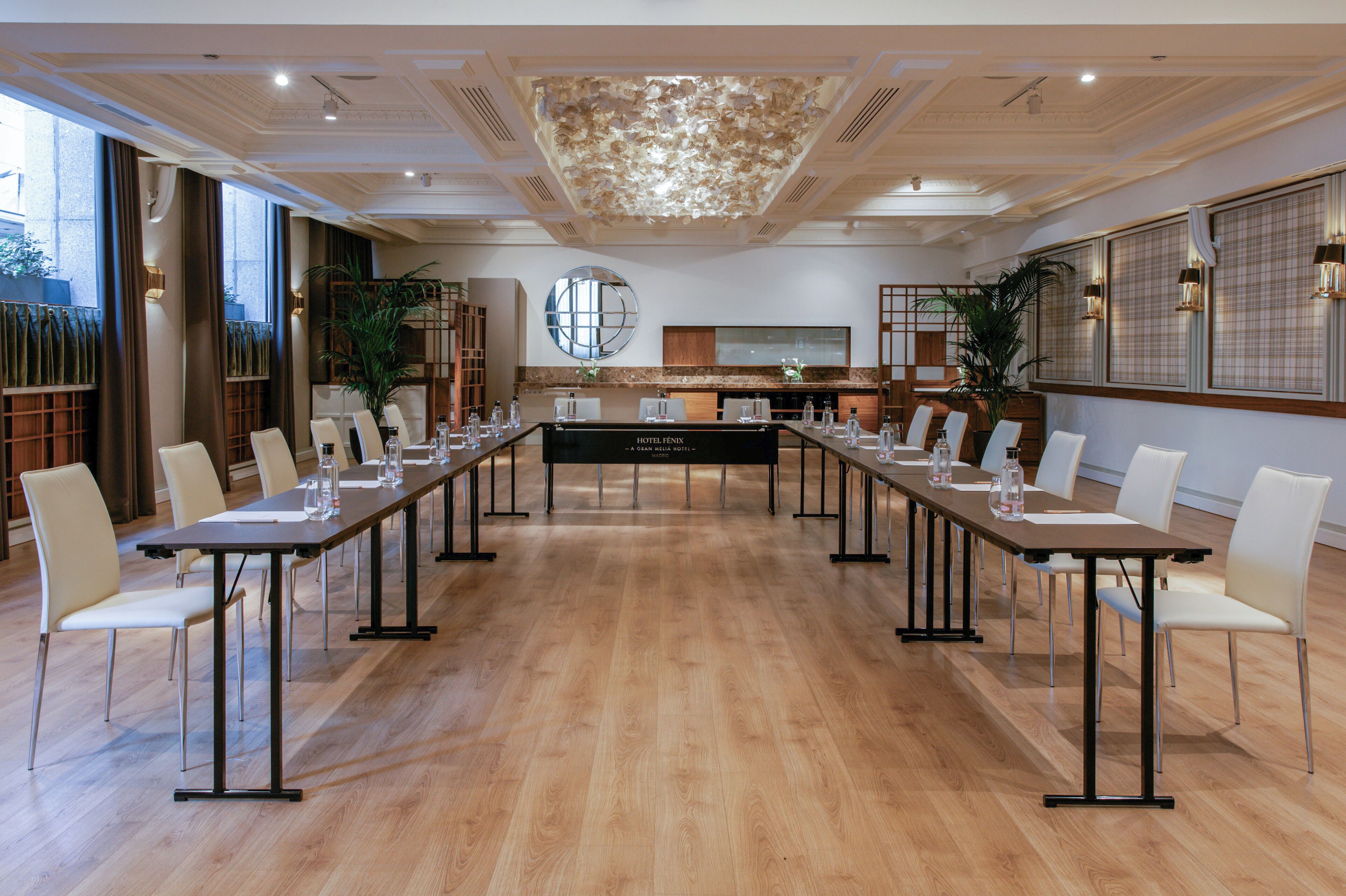 A conference room with a long table, white chairs, and a modern chandelier.