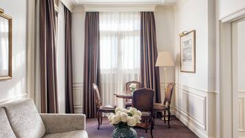 Una habitación de hotel con sofá, una mesa de comedor con sillas, un jarrón con flores y una lámpara.