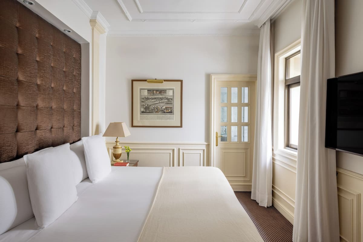 Une chambre d’hôtel avec un grand lit, une télévision, un tableau encadré au mur et une porte avec des rideaux.