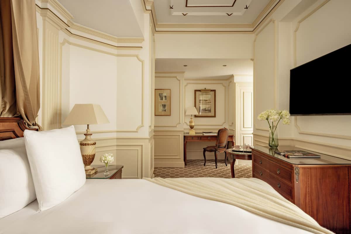 Une chambre d’hôtel avec un grand lit, un bureau, une chaise, une télévision et un vase rempli de fleurs.
