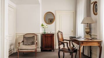 A room with a striped carpet, a wooden cabinet, a round mirror, a table with a lamp, and two chairs.