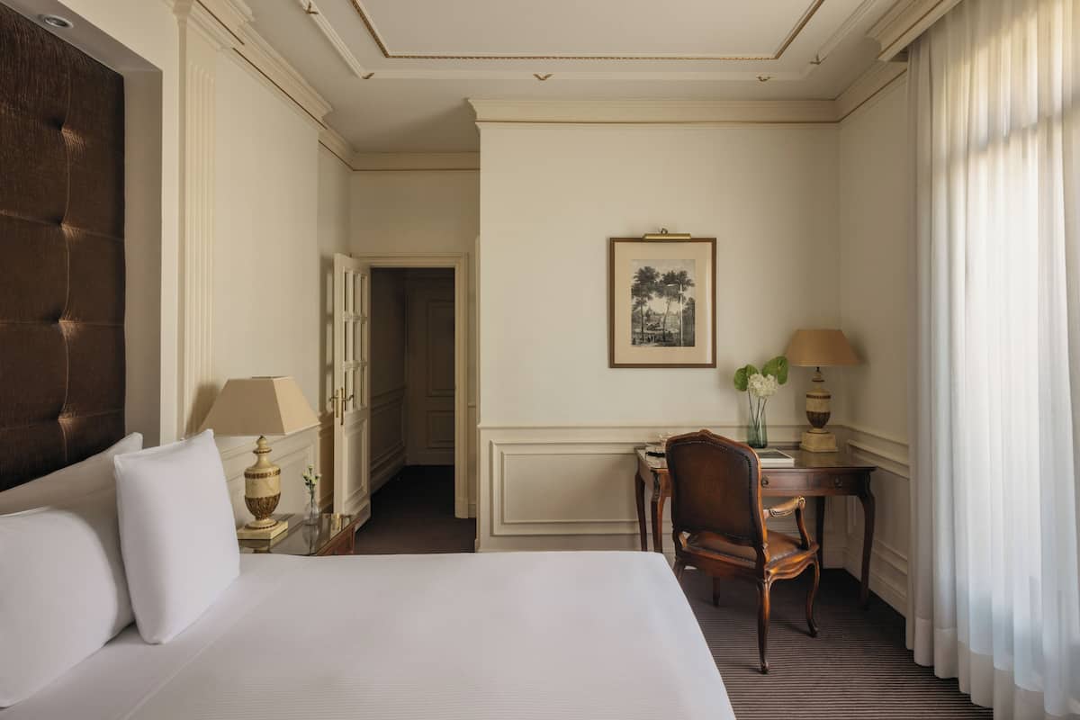 Une chambre d’hôtel avec un grand lit, un bureau avec une lampe, une chaise et un tableau encadré au mur.