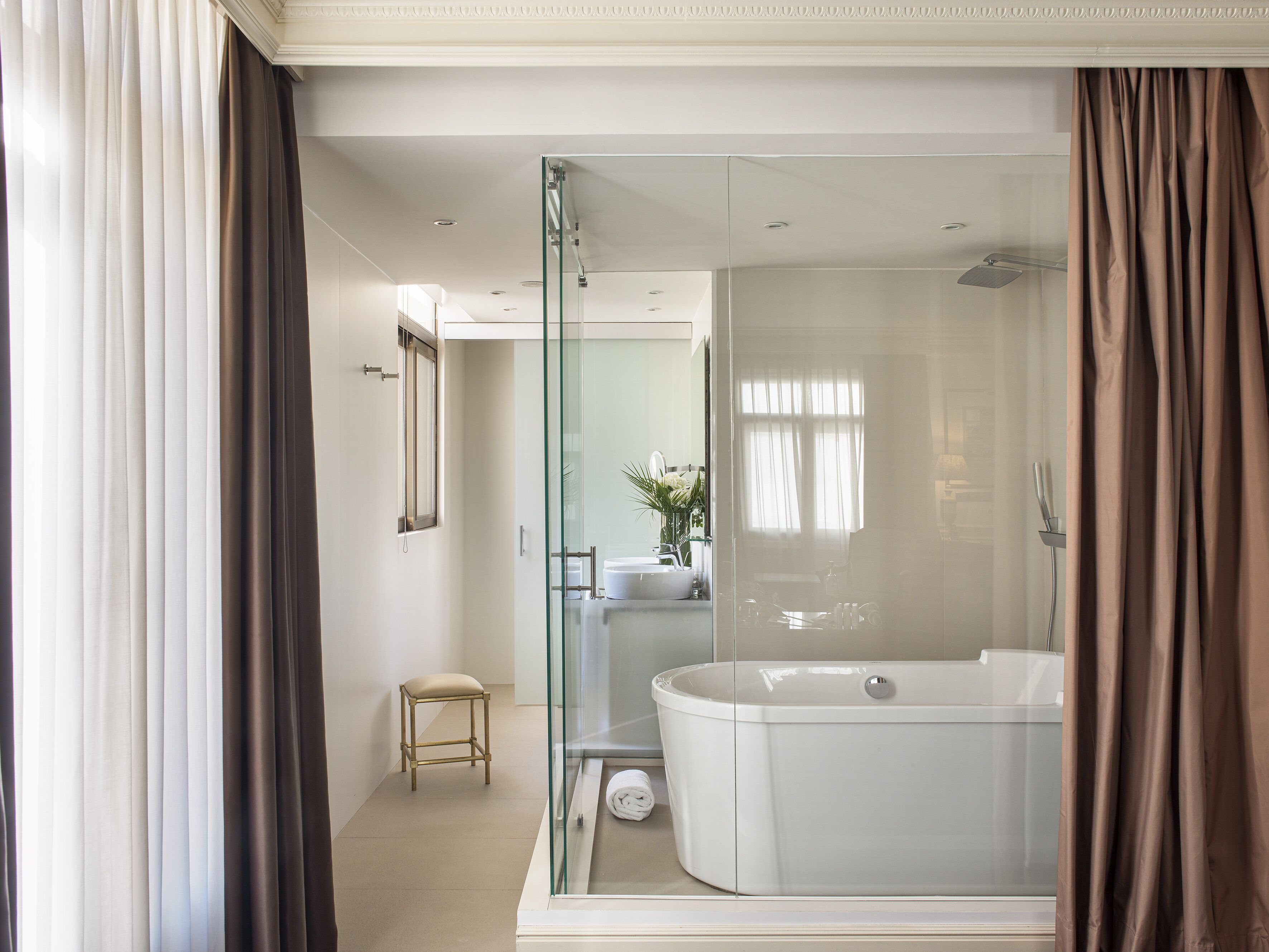 Un baño moderno con ducha de vidrio, bañera independiente y un taburete pequeño.