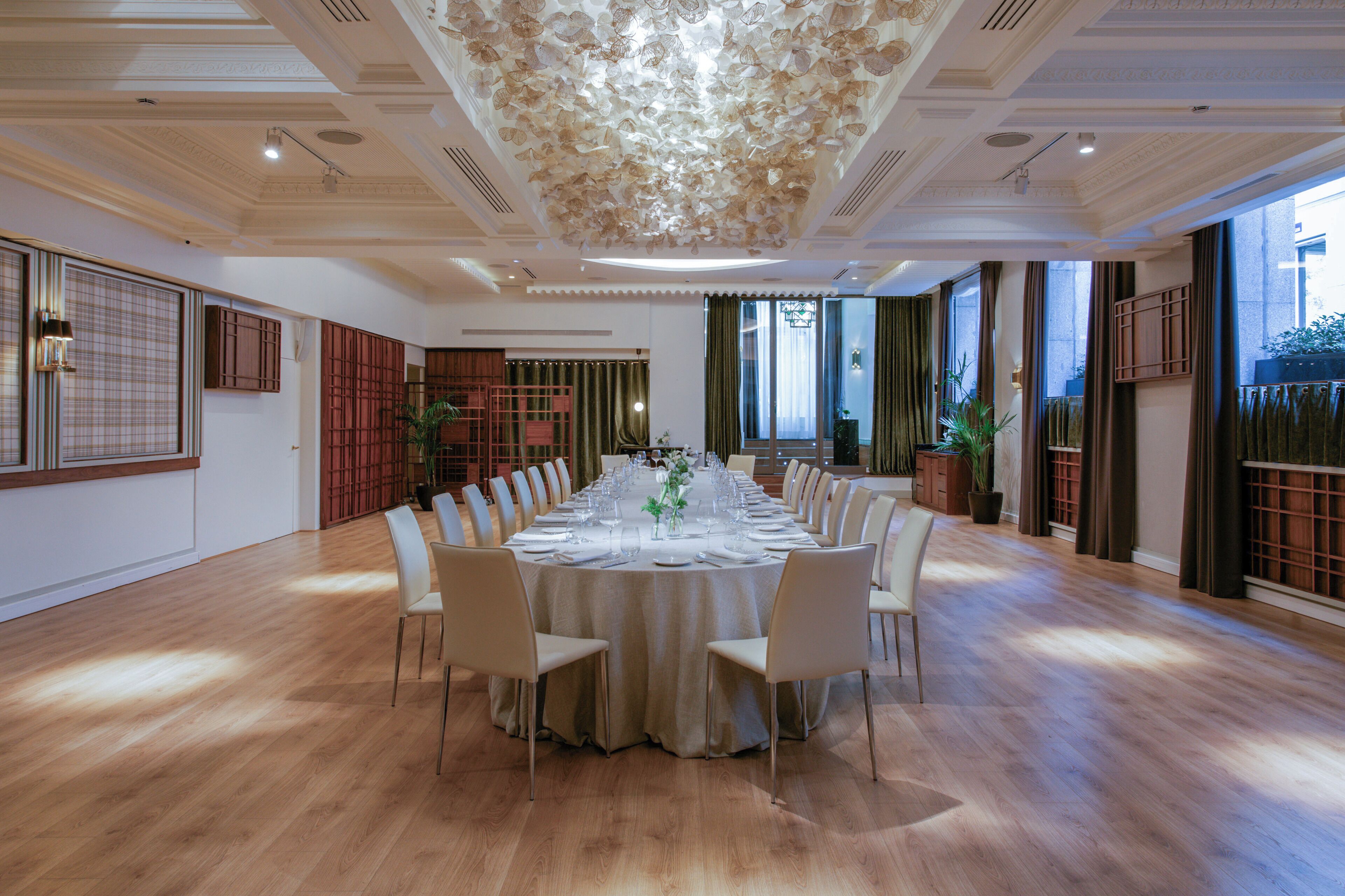 A spacious conference room with a round table, white chairs, and a floral ceiling design.