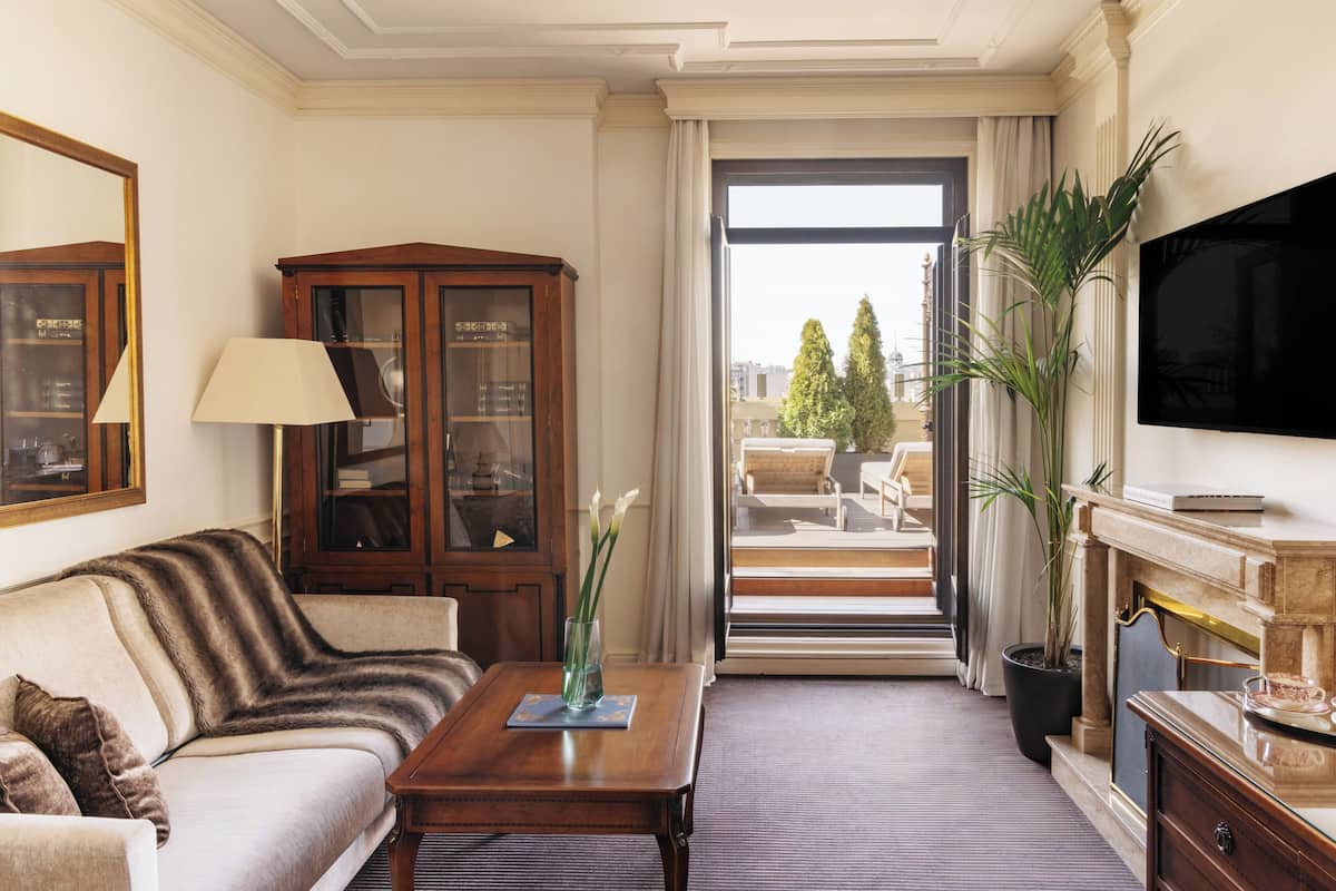 Une chambre d’hôtel avec un canapé, une armoire en bois, une télévision, une cheminée et une vue sur l’extérieur.