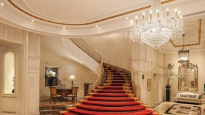 Una gran escalera con alfombra roja, un candelabro y un comedor con mesa y sillas.