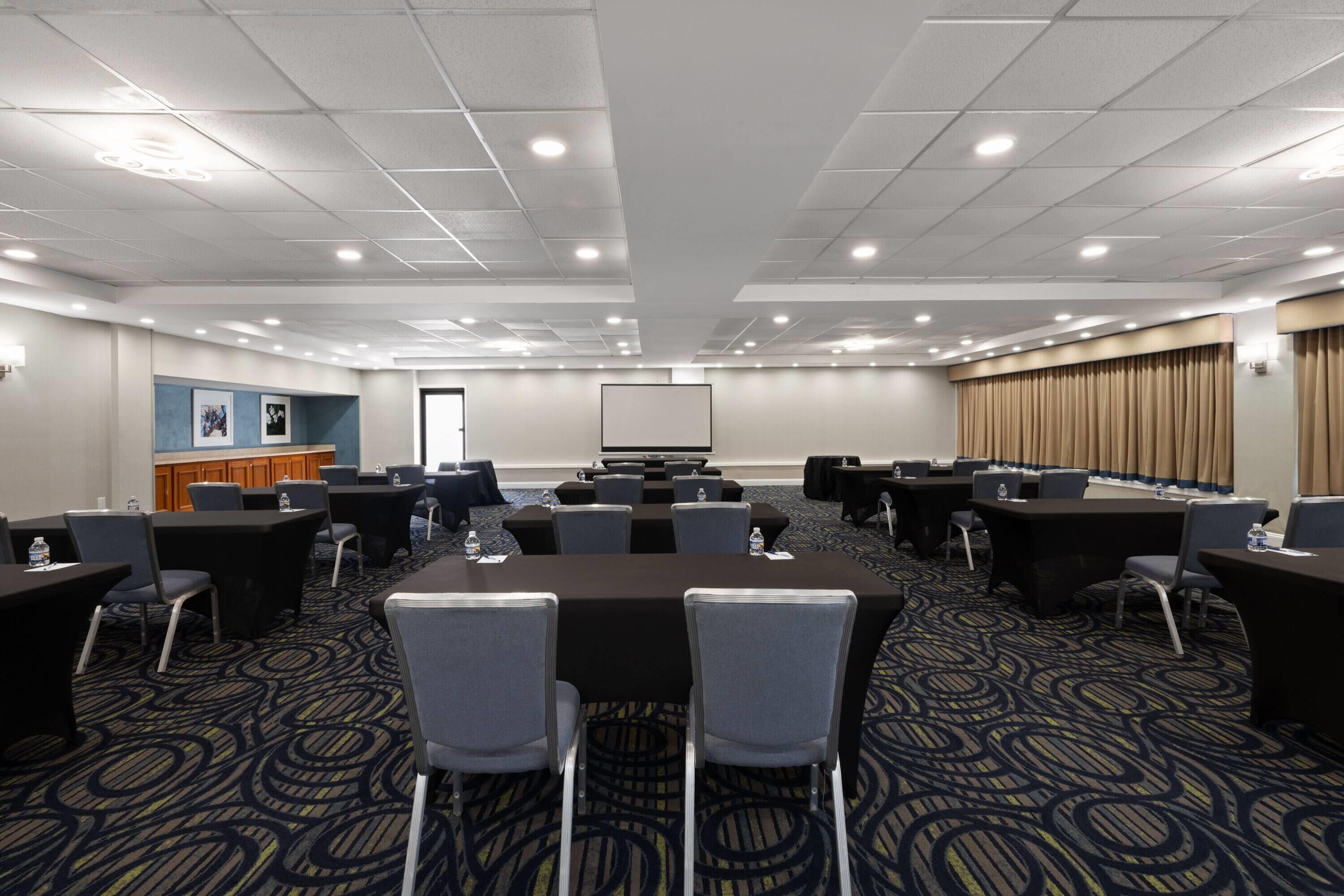 Un salón de conferencias con una gran mesa, varias sillas, una pantalla de proyección y un dispensador de agua.