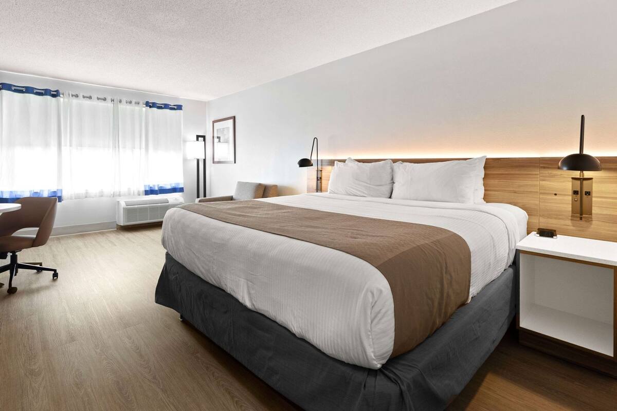 A hotel room with a large bed, a desk, a chair, and a window with curtains.