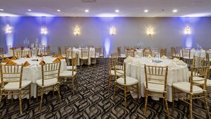 Un salón de banquetes con mesas redondas, manteles blancos y sillas doradas.