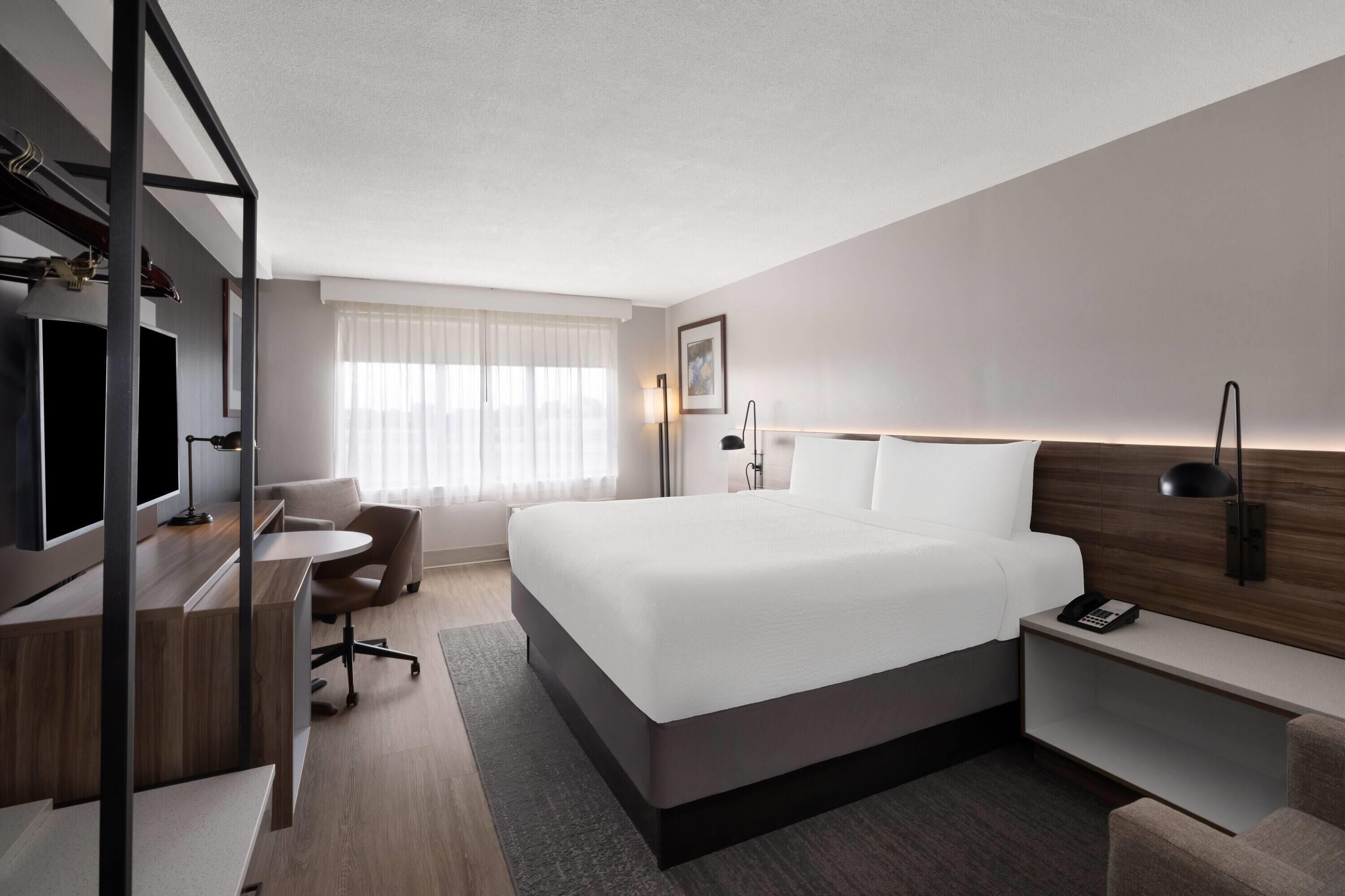 Ein modernes Hotelzimmer mit einem großen Bett, einem Schreibtisch, einem Stuhl, einem Fernseher und einem Nachttisch.