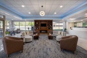 A spacious lounge area with a fireplace, comfortable seating, and a large window providing a view of the outdoors.