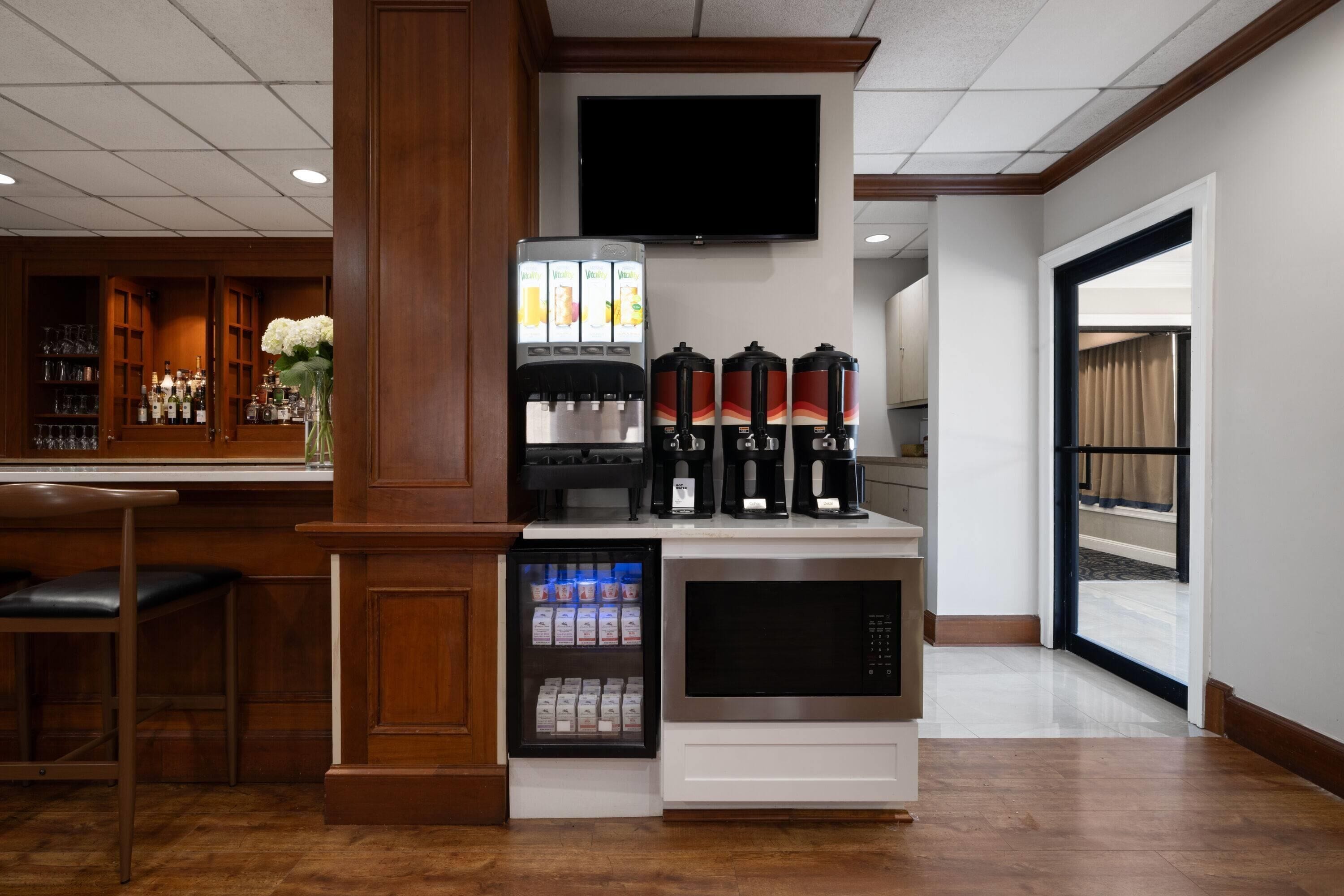 A bar area with a refrigerator stocked with beverages, a coffee machine, and a flat-screen TV mounted on the wall.
